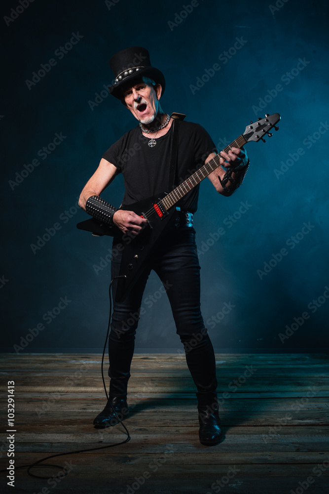 Heavy metal senior man with electric guitar in front of dark blu