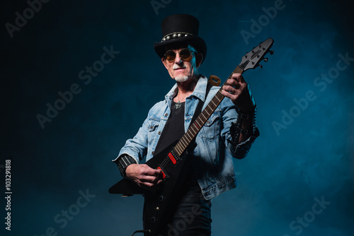 Heavy metal senior man with electric guitar in front of dark blu © ysbrandcosijn