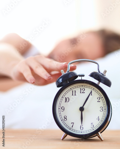 Young sleeping woman and alarm clock in bedroom at home