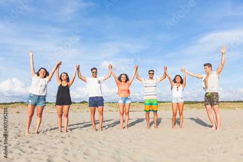 Multiracial group of friends with raised hands on the beach