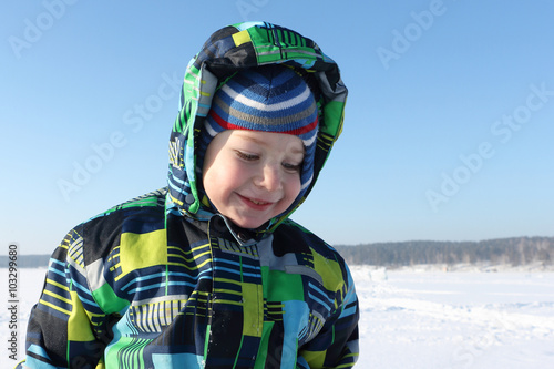 The smiling child in a color jacket with a hood against snow iin the winter 