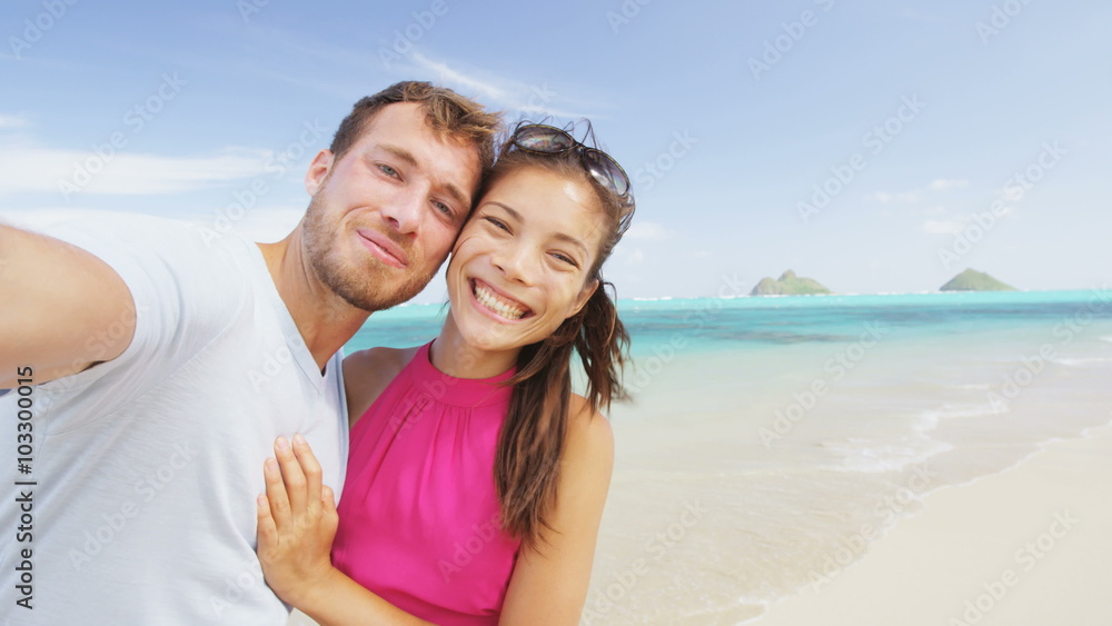 Couple relaxing on beach taking selfie picture with camera smart phone. Young multiracial couple on getaway vacation in Hawaii having fun looking at camera. Candid closeup. RED EPIC SLOW MOTION. Couple relaxing on beach taking selfie picture with camera smart phone. Young multiracial couple on getaway vacation in Hawaii having fun looking at camera. Candid closeup. RED EPIC SLOW MOTION.