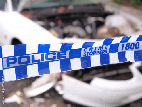 Blue and white Police tape cordoning off a area with a badly accident damaged white car, Australia 2016
