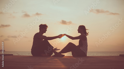 Young couple is doing yoga on the sunrise background.