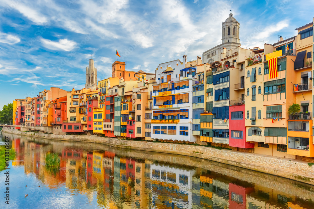 Colorful yellow and orange houses and famous house Casa Maso reflected in water river Onyar, in Girona, Catalonia, Spain. Church of Sant Feliu and Saint Mary Cathedral at background.