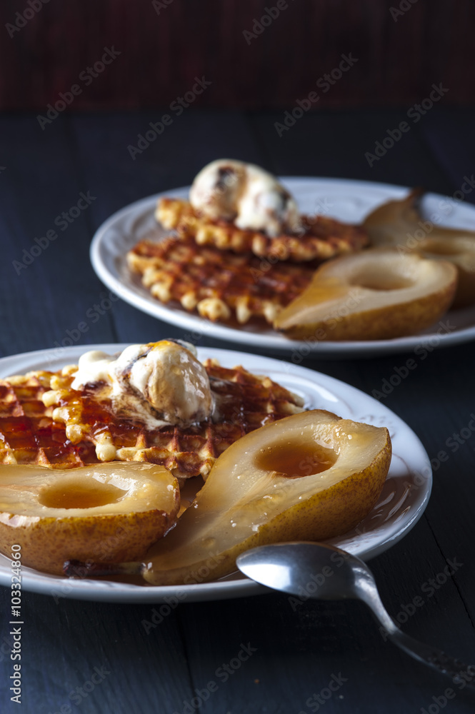 Waffles, pears cooked in sugar syrap and ice cream on white plate, spoons on blue wooden table
