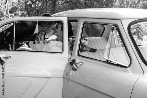 Beautiful brunette bride in retro white car kissing handsome gro