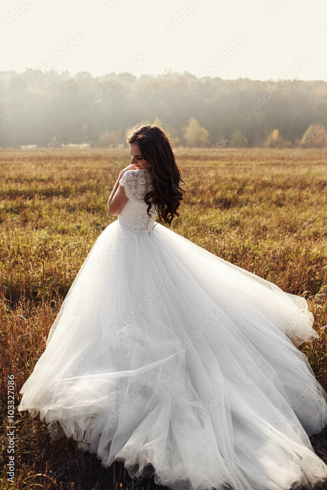 Beautiful happy brunette bride in white dress posing in sunset f
