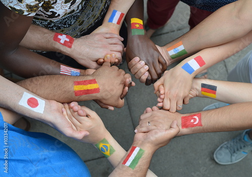 Internationale Brüder und Schwestern mit unterschiedlichen Flaggen auf ihren Armen gemalt stehen miteinander im Kreis und halten sich die Hände. photo