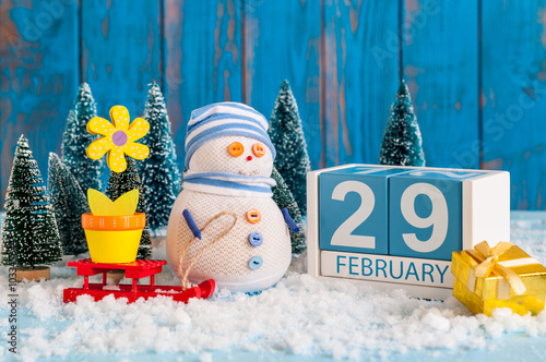 February 29th. Cube calendar for february 29 on wooden surface with snowman, sled, snow, fir and spring flower. Leap year, intercalary day photo