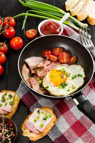 Fried eggs with ham, tomatoes and onion in pan