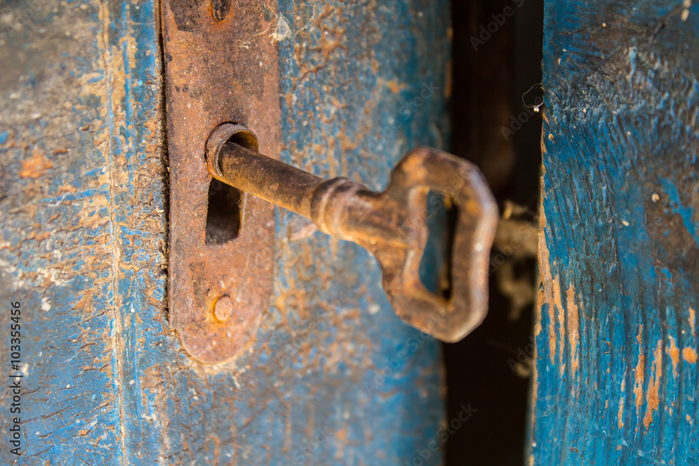 Naklejka premium Old rusty key and keyhole on a blue wooden door