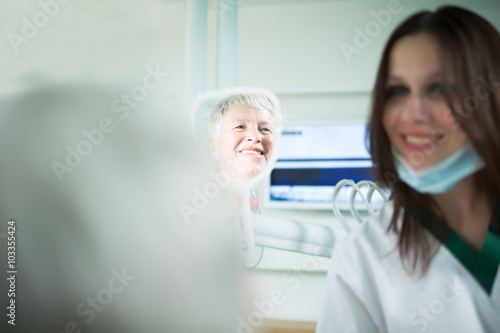 Old woman visiting the dentist taking care of her teeth.Young female dentist showing a granny her teeth reflection in the mirror.Dentist doctor talking to a senior woman patient.Dental care for elder
