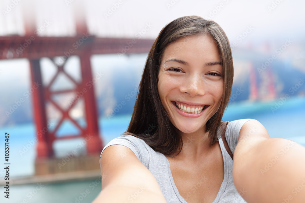 Selfie girl on San Francisco Golden bridge travel. Cute young Asian woman adult taking picture with her smartphone during summer vacation in front of the famous American attraction, California, USA.