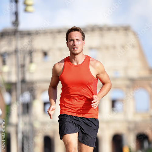 Runner man running at italian city Rome marathon near Colosseum, Roma, Italy. Handsome male athlete training cardio jogging on street with famous touristic attraction landmark in the background. © Maridav