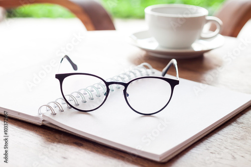 Open blank white notebook and eyeglasses with cup of coffee