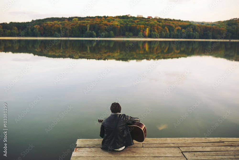Obraz premium Young man playing on guitar at the lake
