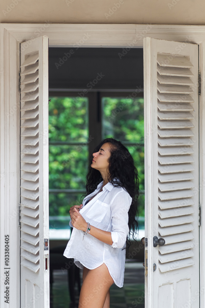 Beautiful woman with long black hair posing near white door Beautiful woman with long black hair posing near white door