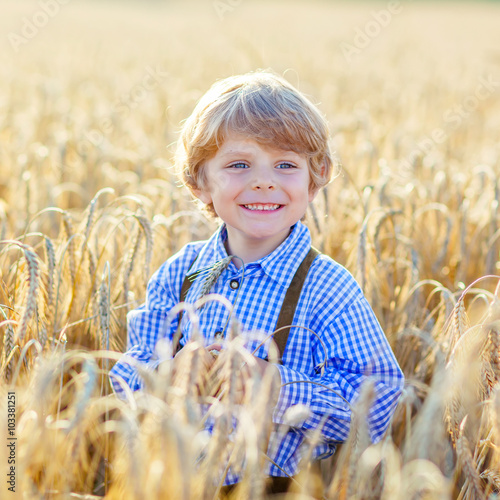 Funny little kid boy in leather shors, walking  through wheat fi photo