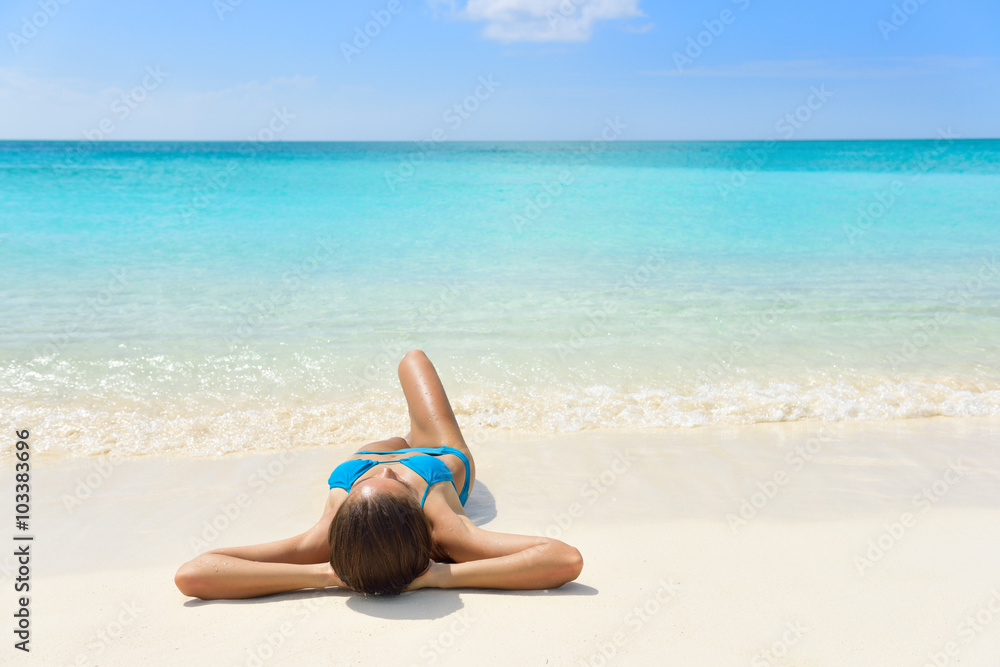 Tropical Caribbean beach vacation - suntan relaxation woman. Bikini girl lying down relaxing on white sand exotic destination sleeping and sunbathing during summer holidays.