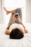 Brunette lying on bed and using smartphone