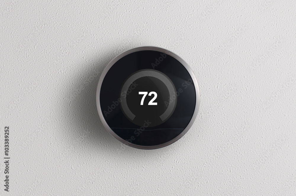 A simplistic photo of a round, modern, programmable digital thermostat, on a clean white wall. A simplistic photo of a round, modern, programmable digital thermostat, on a clean white wall.