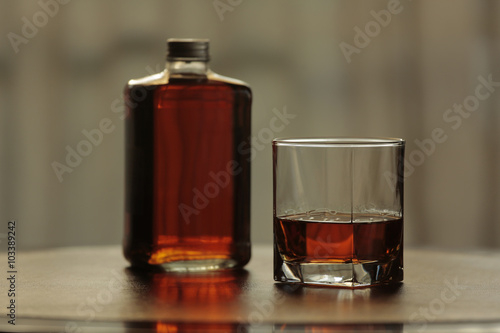 Bottle and glass with whisky together on leather and mahogany table