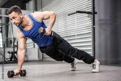Muscular man doing push up with dumbbells