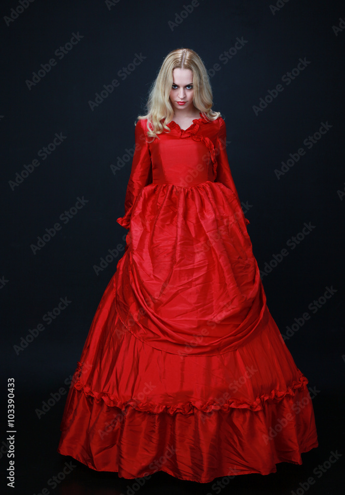 full length portrait of a beautiful blonde woman wearing a historical red silk, victorian era ball gown.