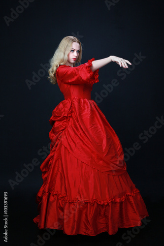 full length portrait of a beautiful blonde woman wearing a historical red silk, victorian era ball gown.