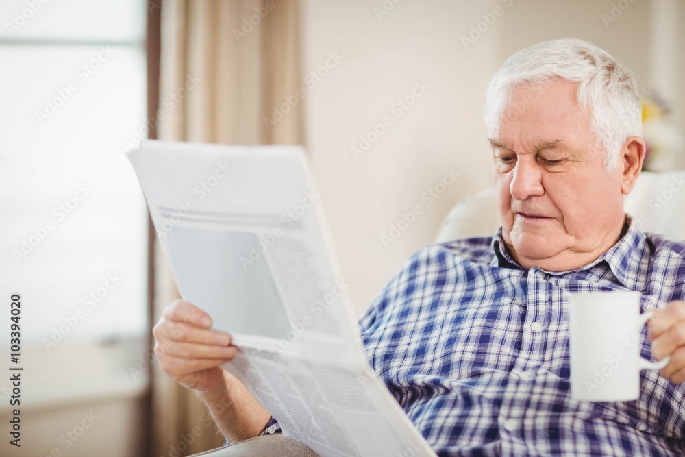 Senior man reading newspaper in living room Senior man reading newspaper in living room