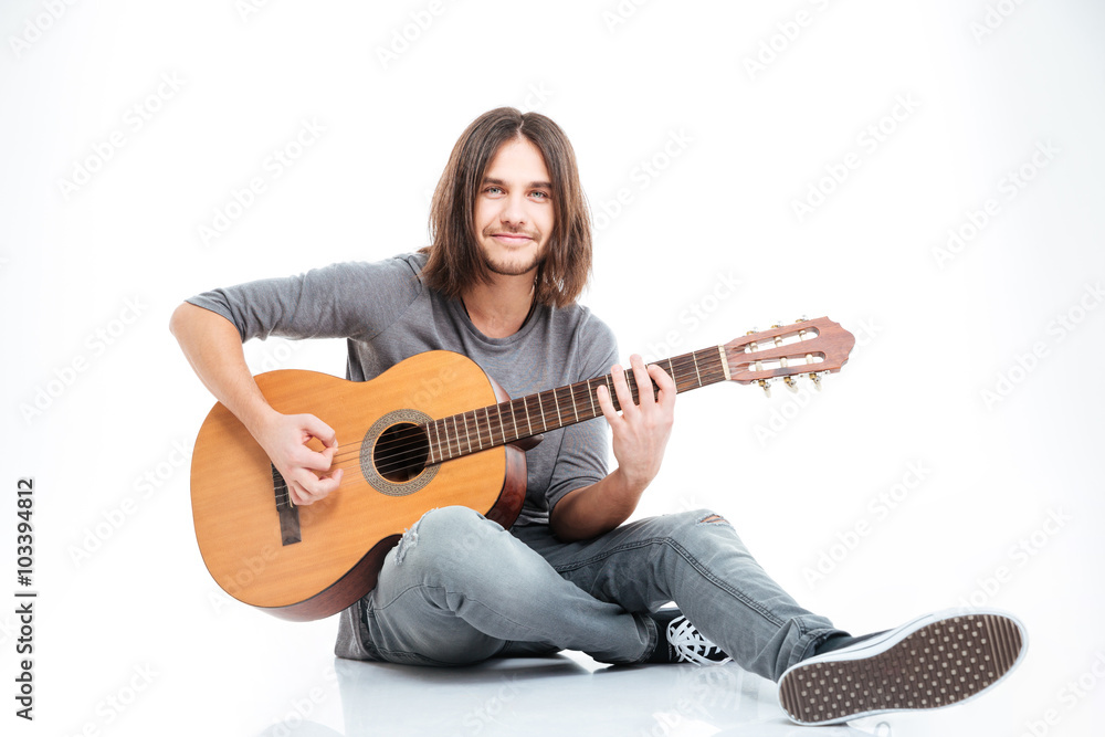 Smiling young man sitting on the floor and playing guitar Smiling young man sitting on the floor and playing guitar