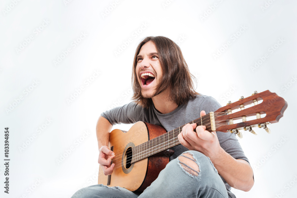 Happy young man with long hair playing guitar and singing Happy young man with long hair playing guitar and singing