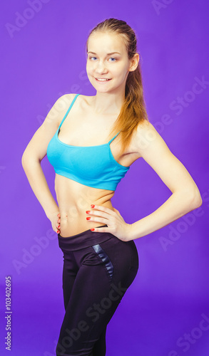 young girl stands and put his hands on the sides on blue background. Fitness, workout, exercise