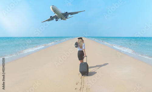 Travel concept. Young woman in flight attendant clothes walking on the beach with suitcase and hat . Overhead fly plane.