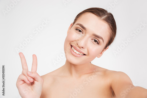 Cheerful young woman making selfie and showing peace sign