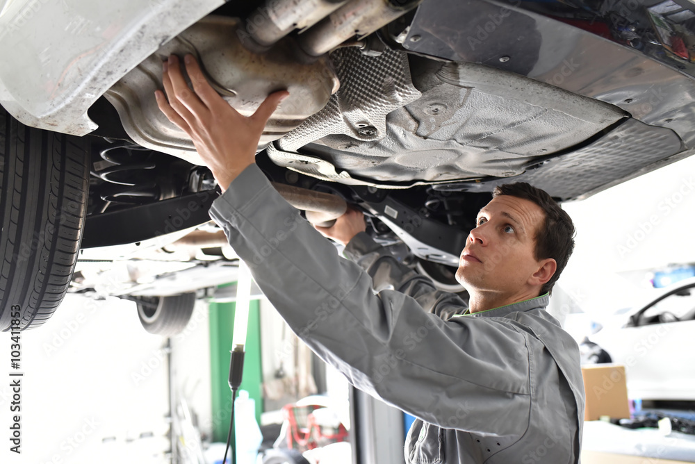 Mechaniker in einer Autowerkstatt kontrolliert Abgasanlage / Endschalldämpfer / Dieselpartikelfilter eines Fahrzeuges - obrazy, fototapety, plakaty 