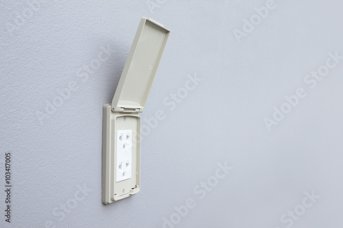 Outdoor electrical outlet with cover on cement wall.