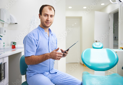 Young male surgeon in uniform sitting in the room in dental clinic with x-ray of a patient. Concept of toothache and teeth cure.  © Stasique