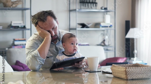 Young tired man with small kid on knee sleeping by table in the morning
