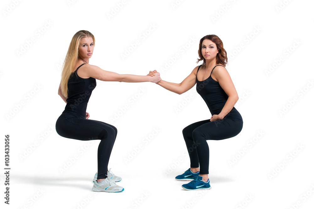 Two women doing squats helping each other isolated Two women doing squats helping each other isolated