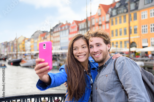 Copenhagen travel people taking friends selfie picture photos as souvenir with smartphone camera. Couple of tourists in the old port Nyhavn, famous Scandinavian attraction in Denmark, northern Europe.