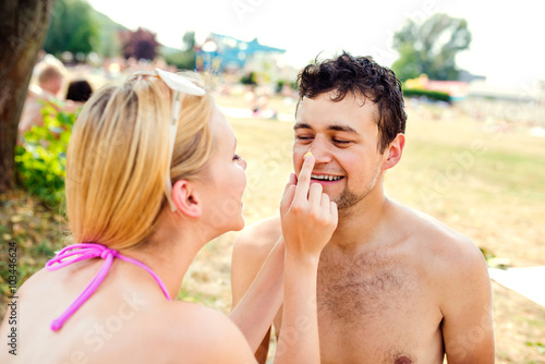 Woman in bikini putting sunscreen on nose of man