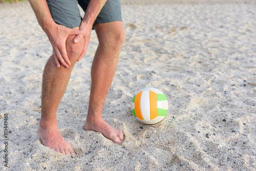 Injuries - sports knee injury on man playing beach volleyball. Male beach volley ball player with pain, maybe from sprain knee. Close up of legs, muscle and knee outdoors.