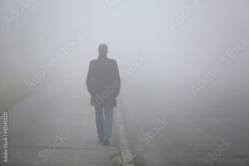 Man with his back walking through the fog street