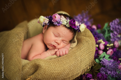 Beautiful newborn baby girl with a purple wreath sleeps in a wicker basket