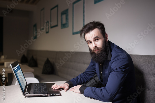 bearded man in suit and with laptop sitting in cafe and browsing © goami