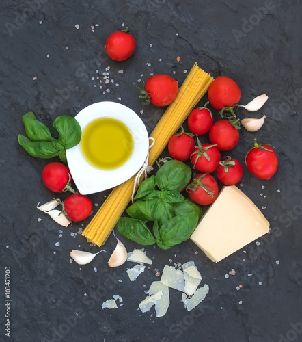 Ingredients for cooking pasta. Spaghetti, olive oil, garlic, Parmesan cheese, tomatoes and fresh basil on black slate background