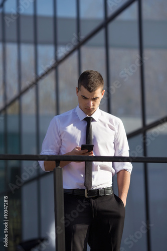 Young businessman using mobile phone in front of the office building