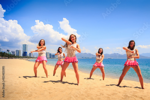 cheerleaders dance crossing arms on beach against resort